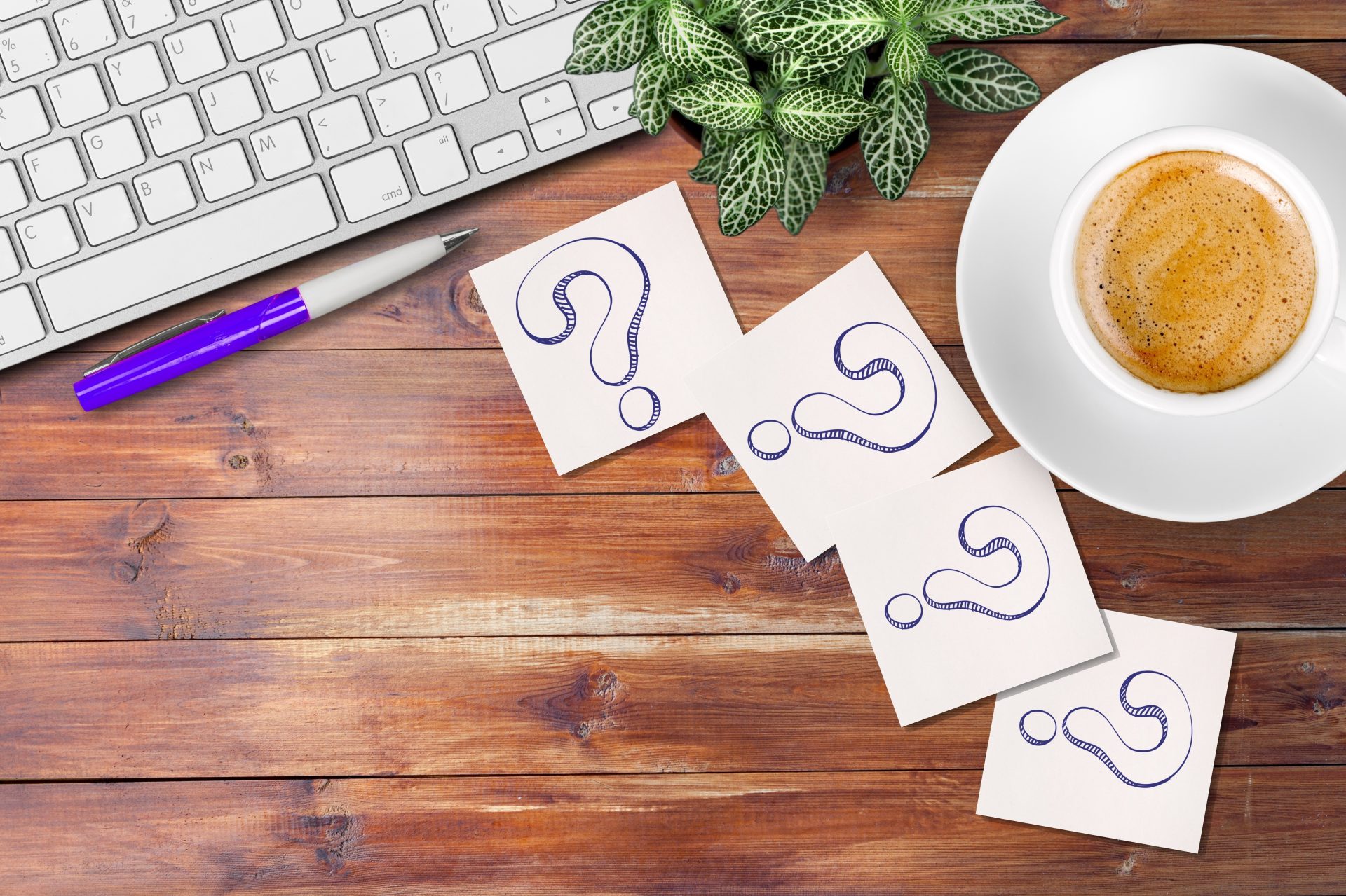 drawing of a question mark on pieces of paper, on a wooden table with coffee and a keyboard in the foreground